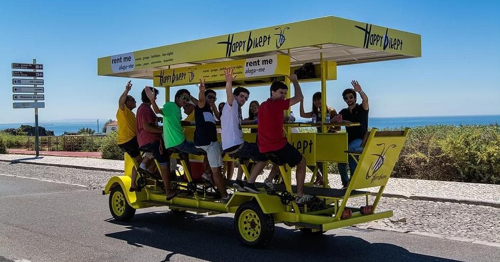 Passengers pedaling beer bike along coastal road in Lisbon