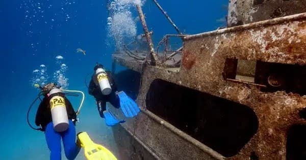 Scuba divers exploring rusted shipwreck in clear blue ocean