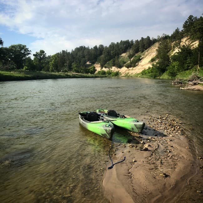 Two kayaks pulled ashore on a sandy riverbank below bluffs