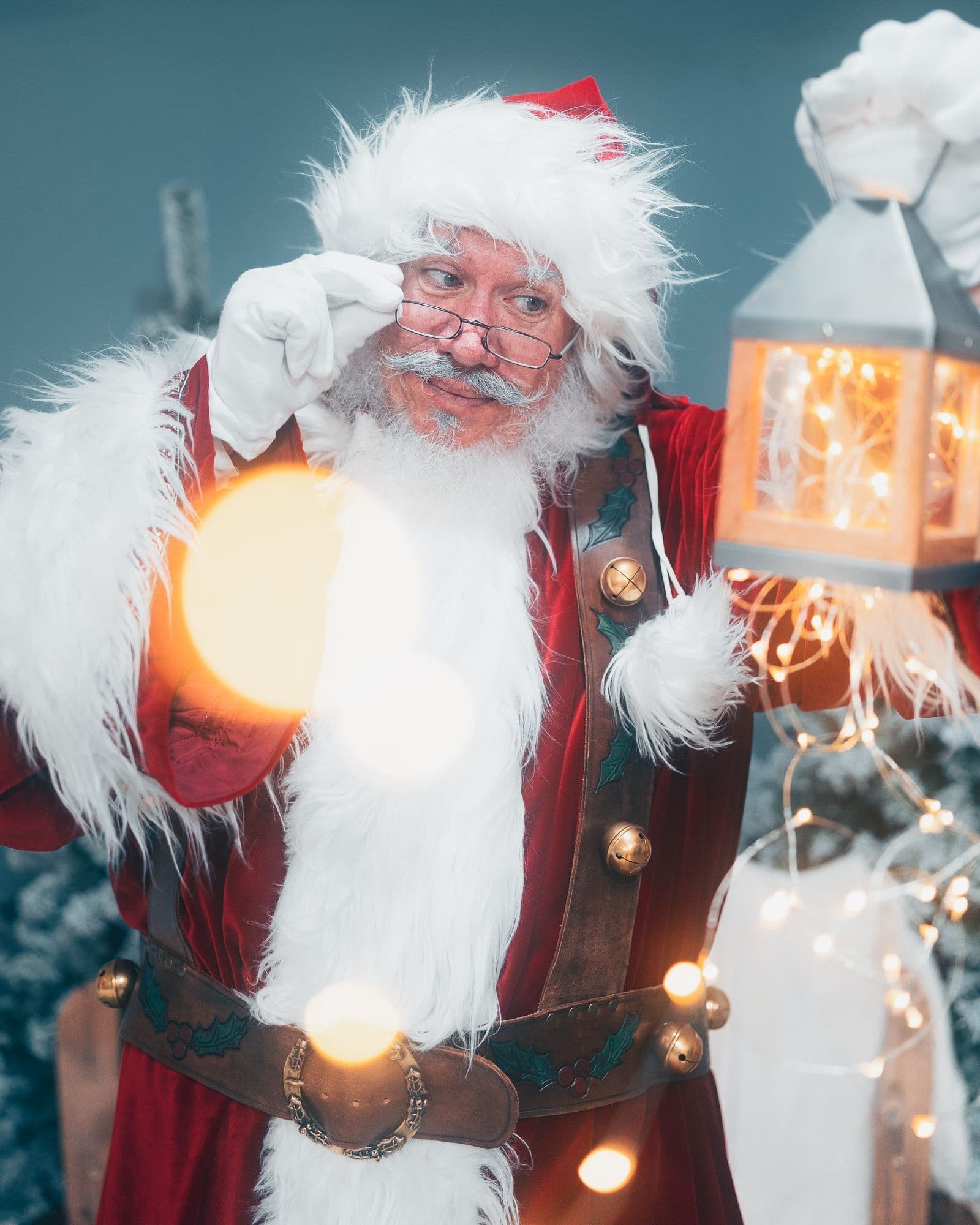 Santa holding lantern amid holiday lights in studio portrait
