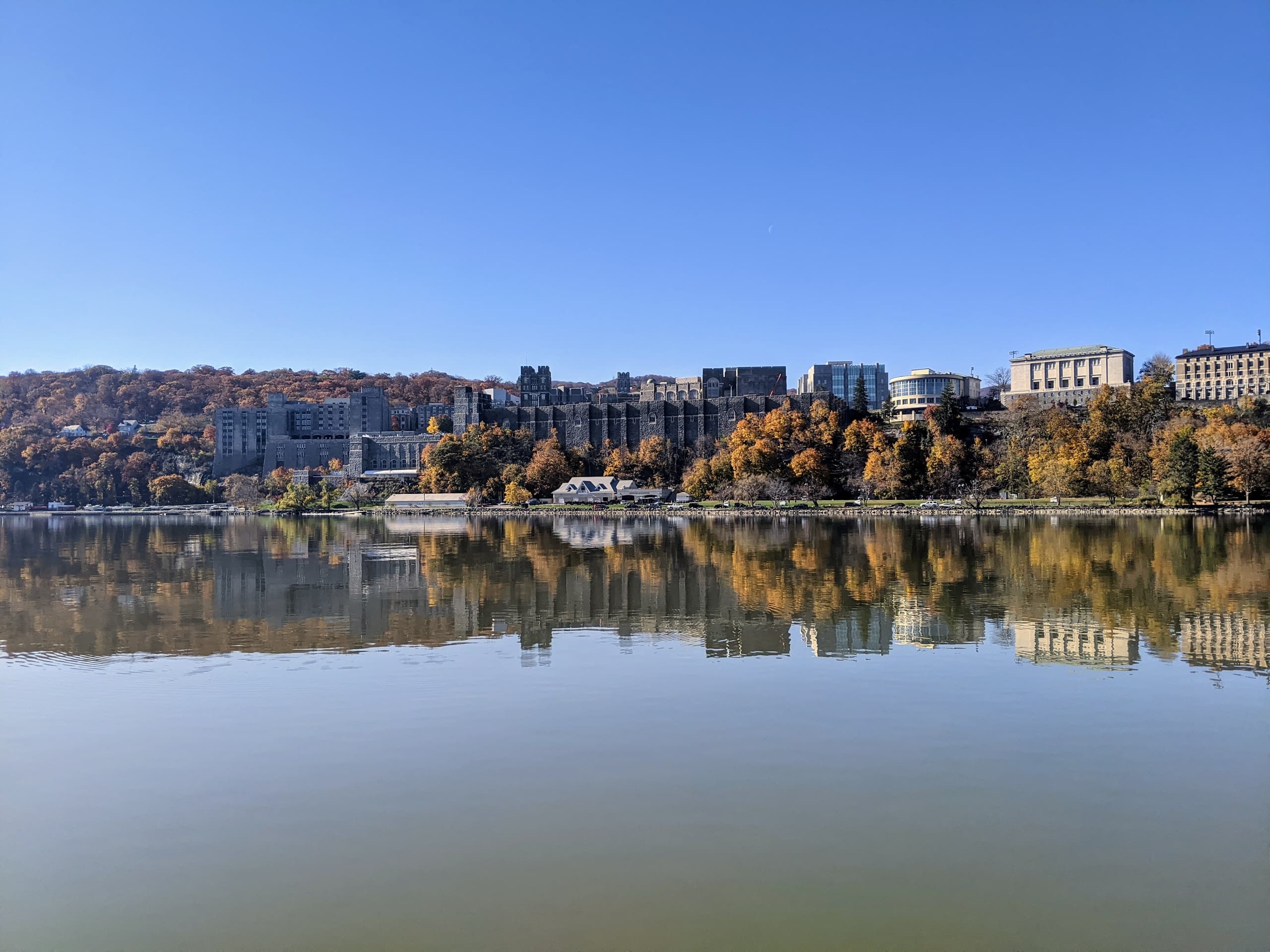 Riverside city skyline reflected in calm water, autumn foliage