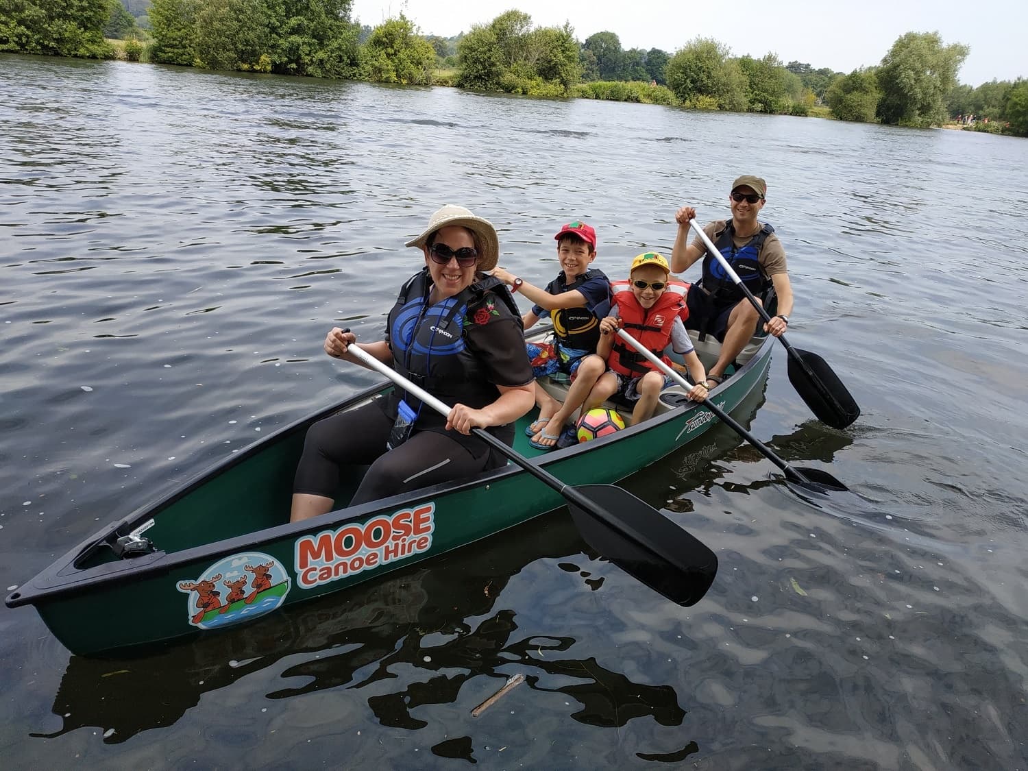 Family canoeing on calm river with children paddling and smiling