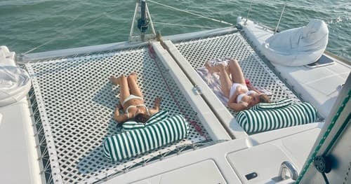 Couple sunbathing on catamaran trampoline over turquoise ocean