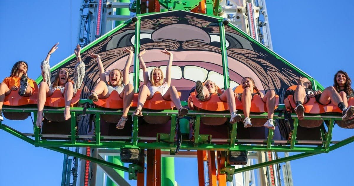 Thrill drop tower riders suspended against blue sky at amusement park