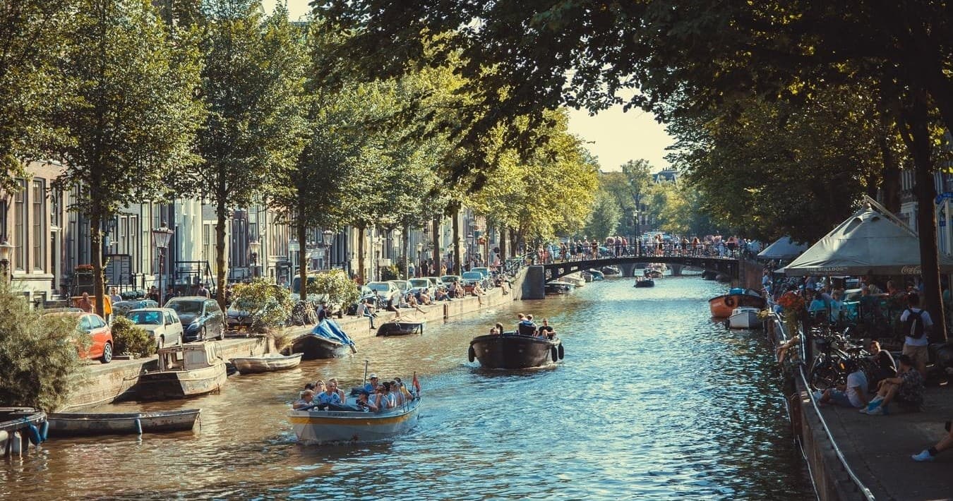 Busy canal with tour boats under shady trees in Amsterdam
