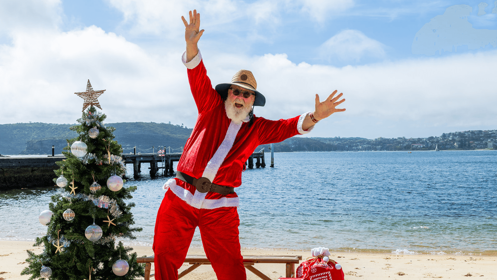 Santa on sandy beach beside Christmas tree at coastal headland
