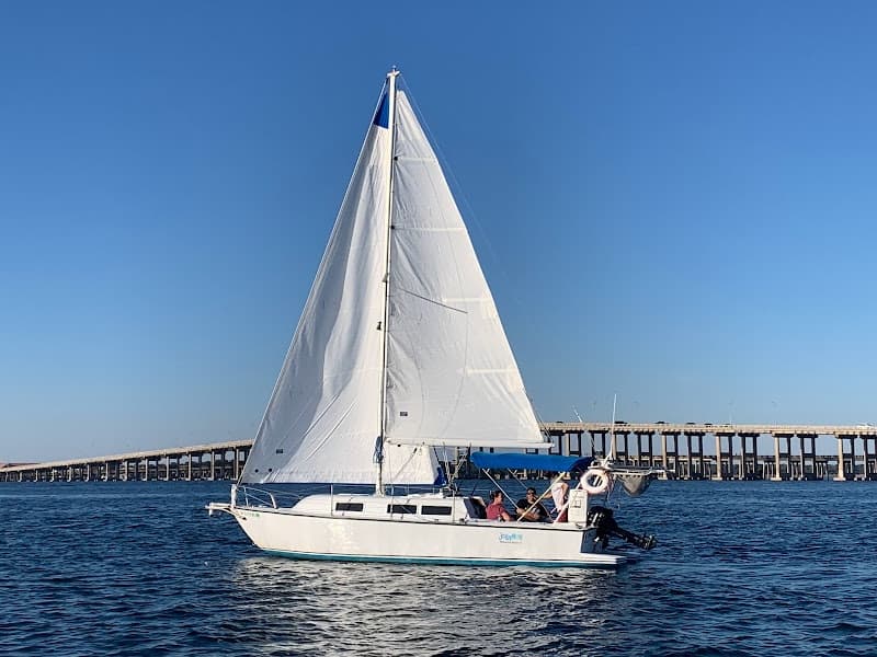Sailboat cruising near coastal bridge under bright blue sky