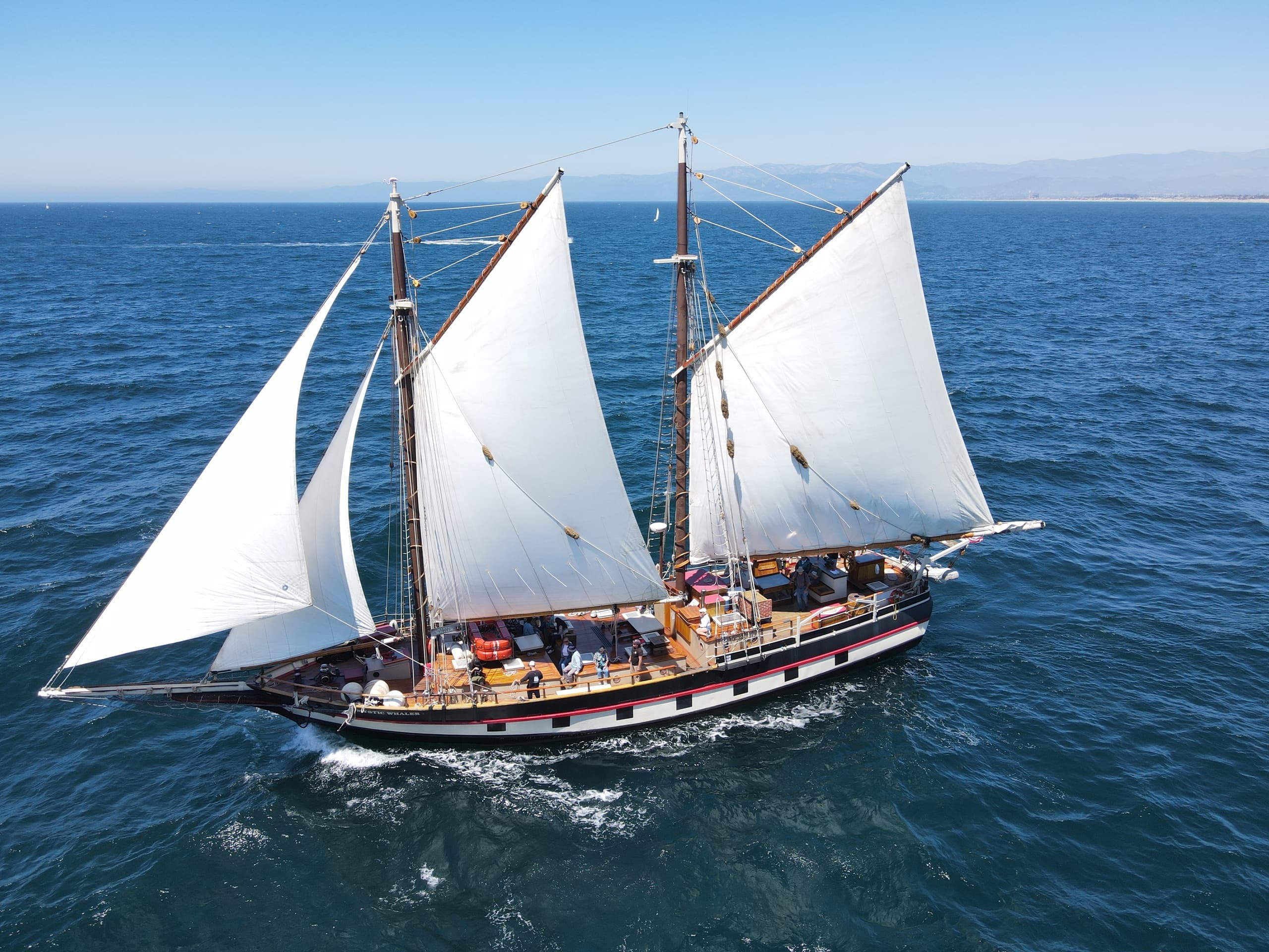 Two-masted schooner sailing on bright blue ocean near coast