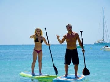 Couple stand-up paddleboarding on calm blue sea near shore