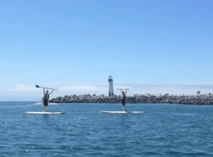 Two paddleboarders cruising near coastal lighthouse on ocean