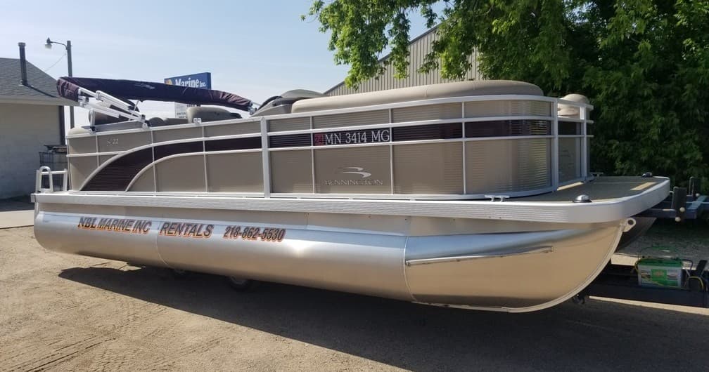 Family pontoon boat parked on pavement under trees, ready to rent