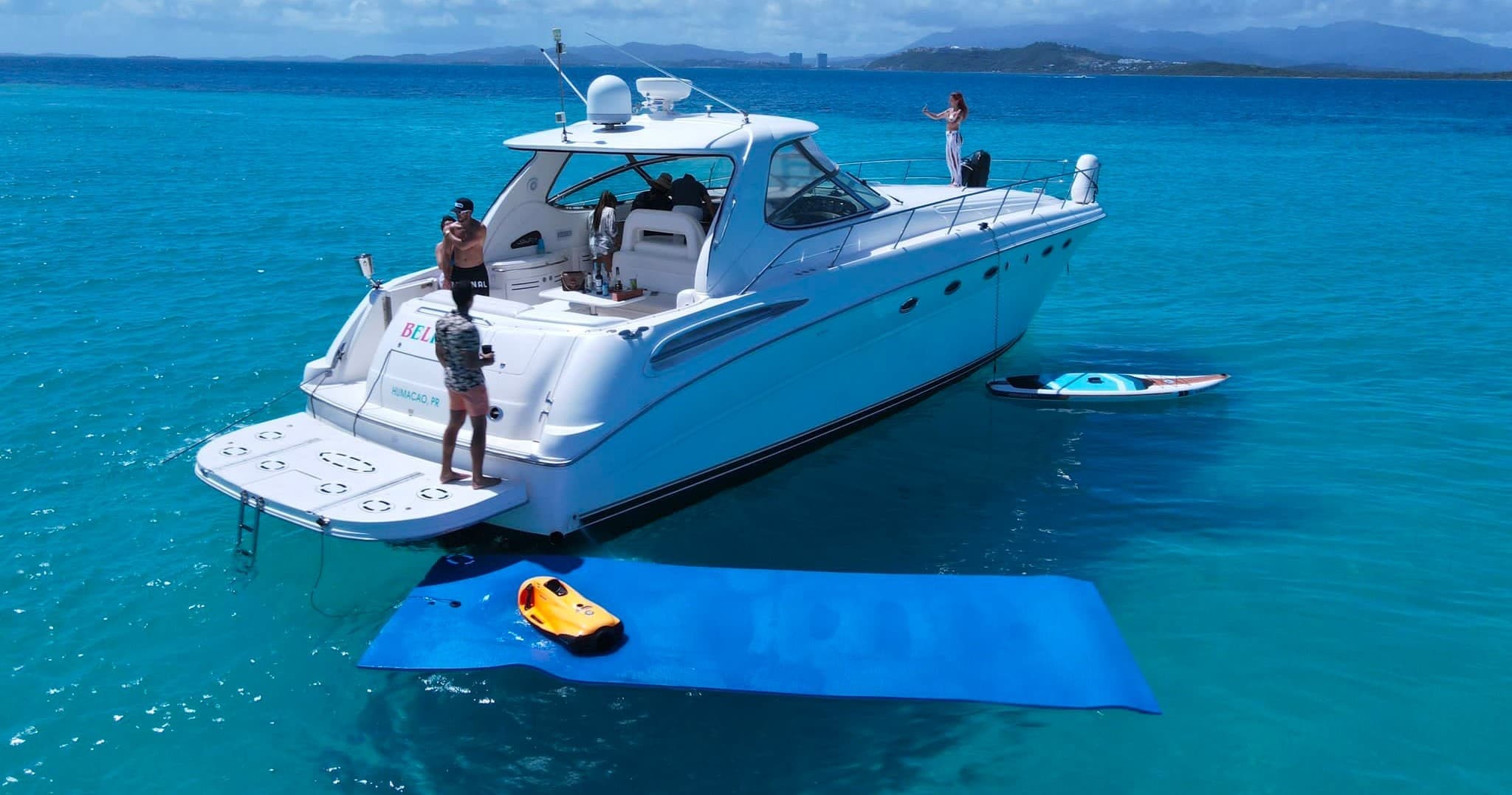 Yacht anchored over shallow turquoise reef with paddleboard and mat