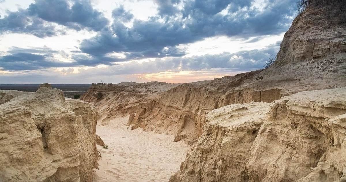 Eroded sandstone canyon trail under dramatic cloudy sky