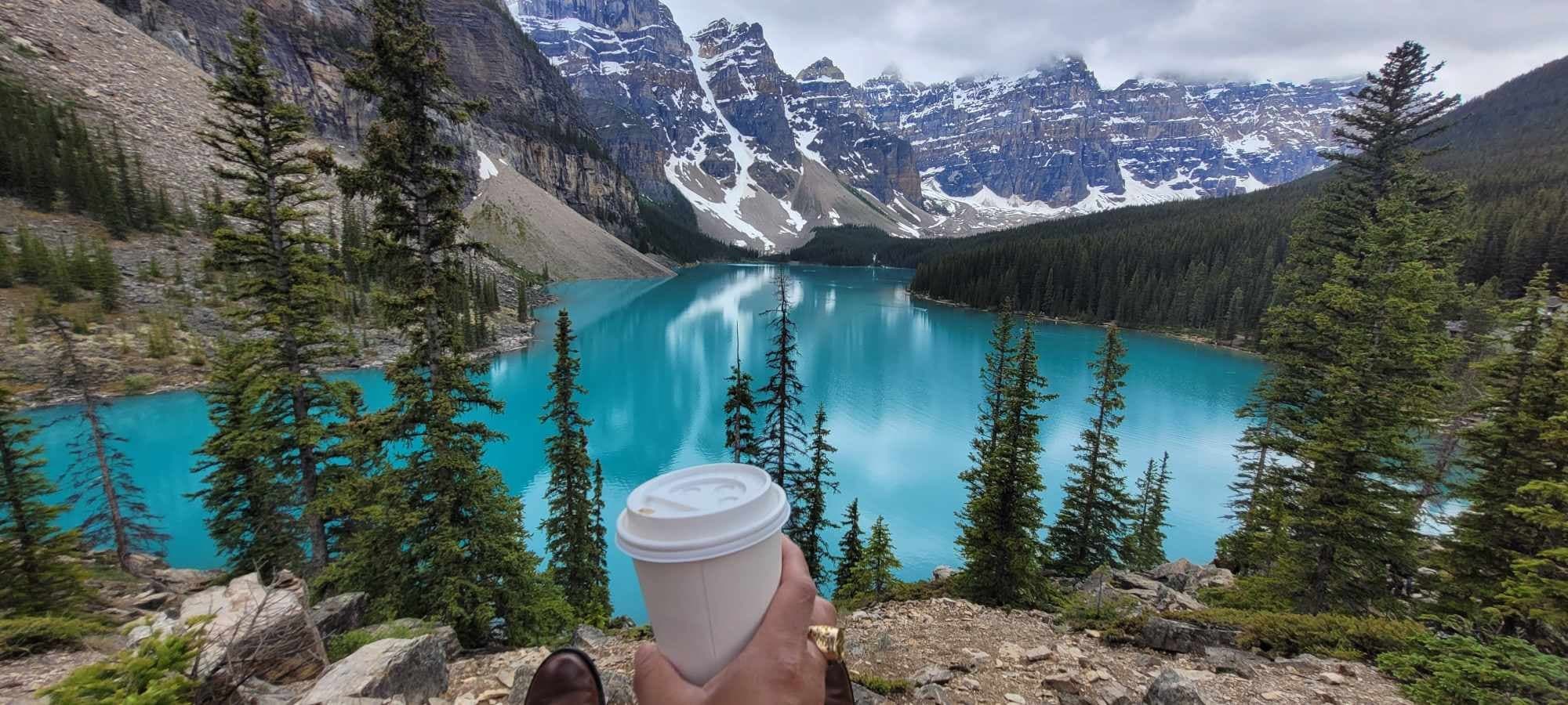 Hiker with coffee overlooking turquoise Moraine Lake, Banff NP