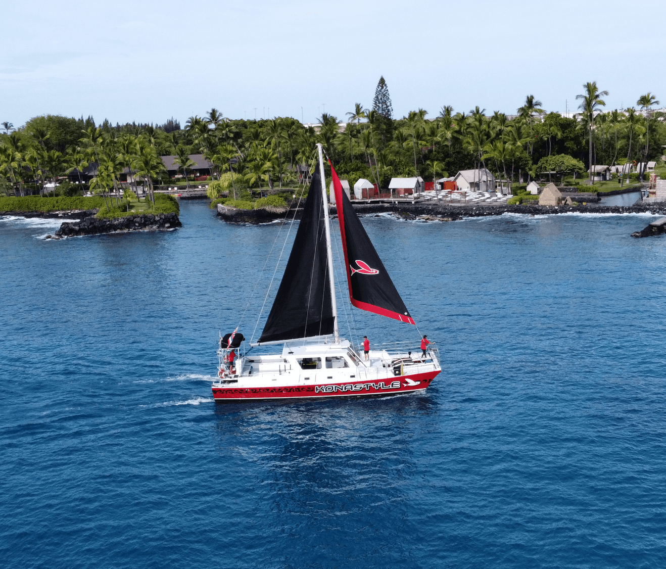 Red-and-white sailboat cruising coastal waters near lush shoreline