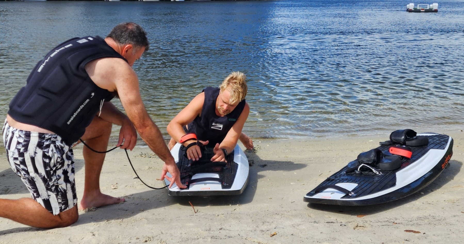 Instructor assists rider prepping electric surfboard on sandy beach