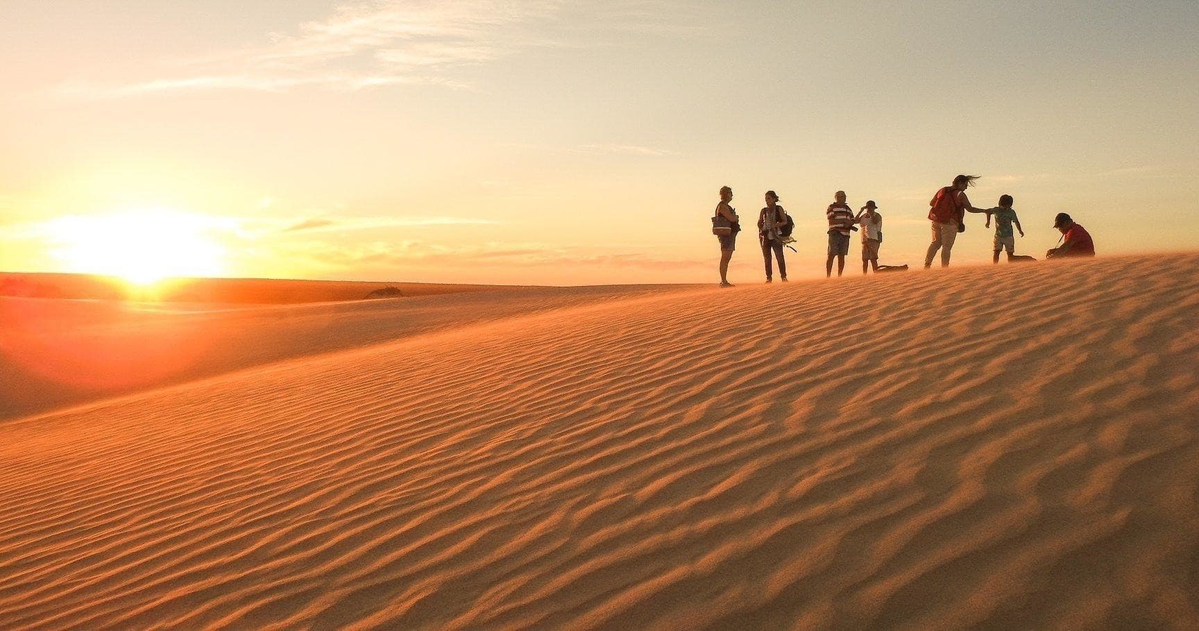 Group hiking on sand dunes at sunset, desert landscape tour