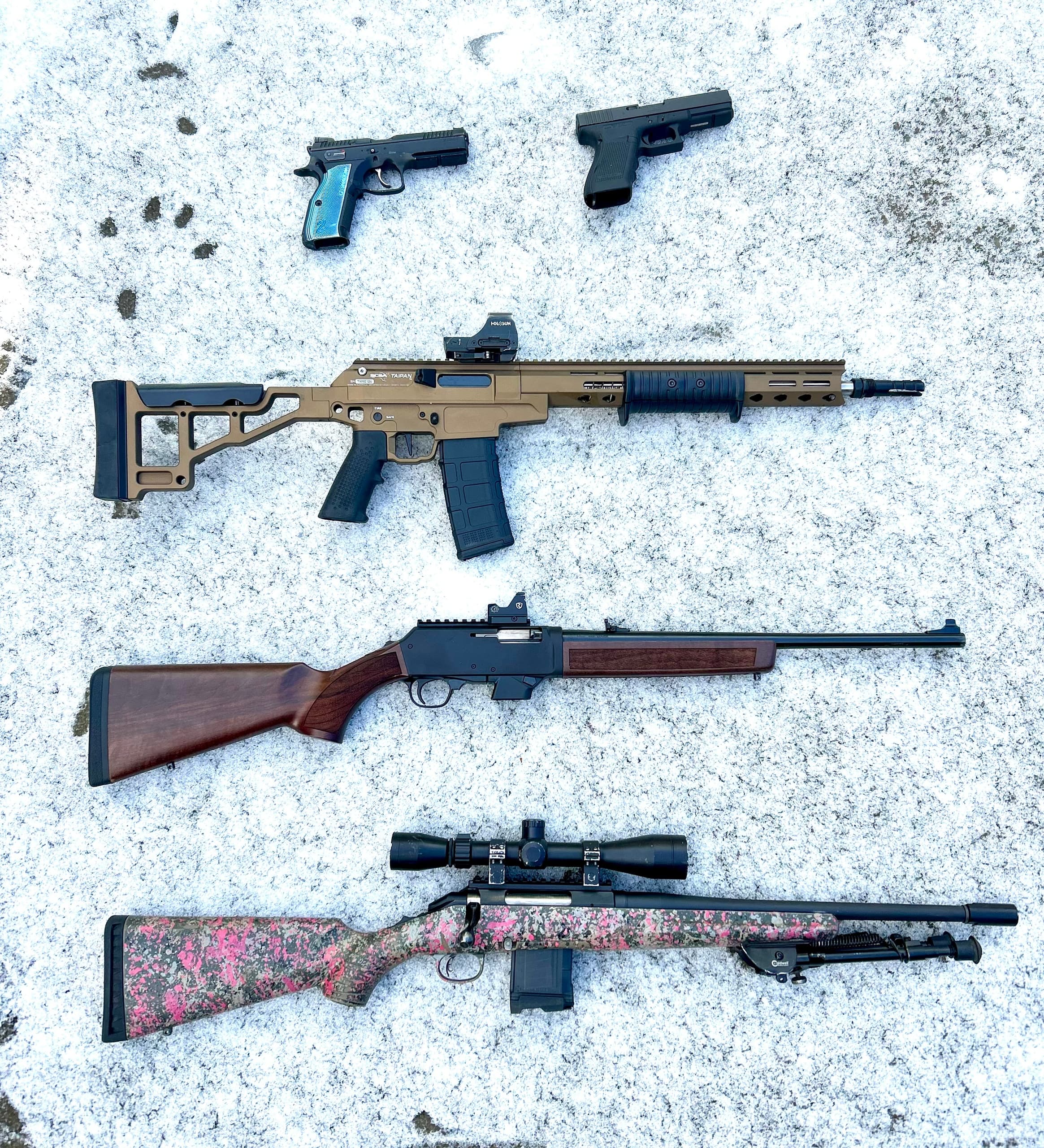 Assorted rifles and pistols laid on snowy ground, gear display