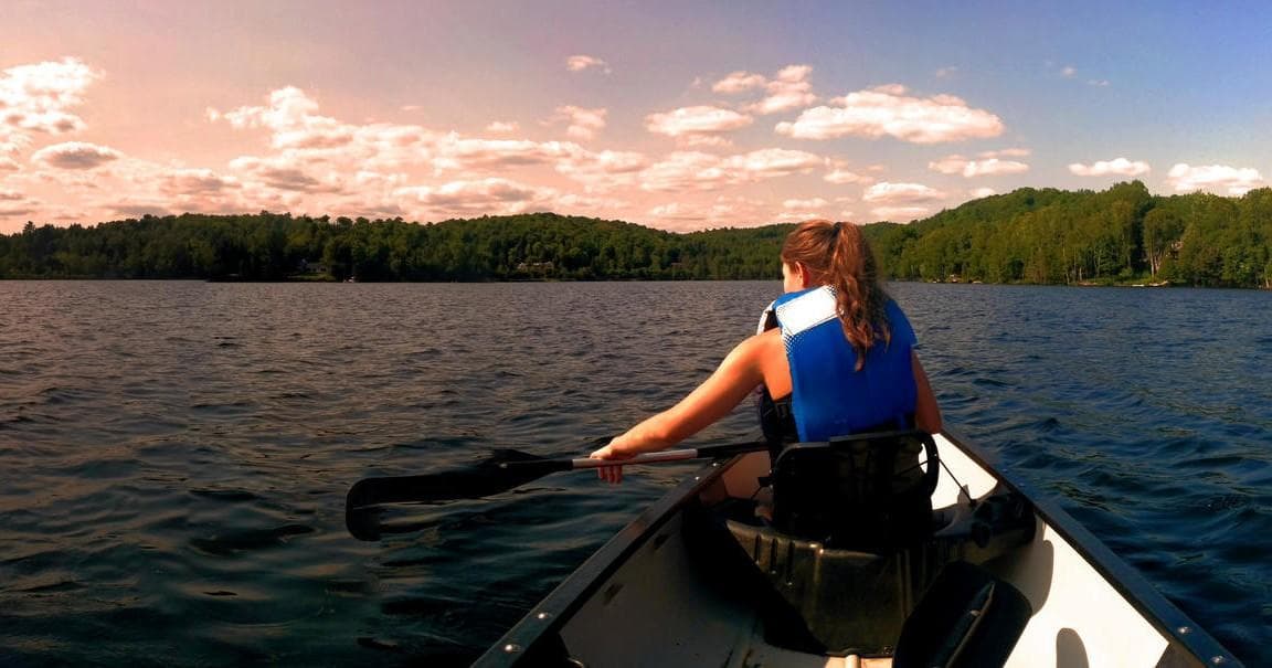 Solo canoeist paddling across serene lake under sunset sky