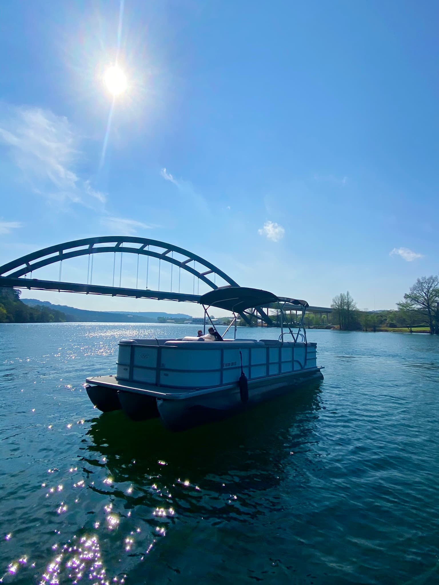 Pontoon boat cruising on sunny lake near arched bridge