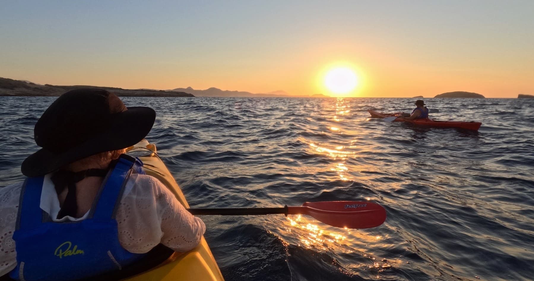 Kayaker paddling at sunset on open sea off coastal islands