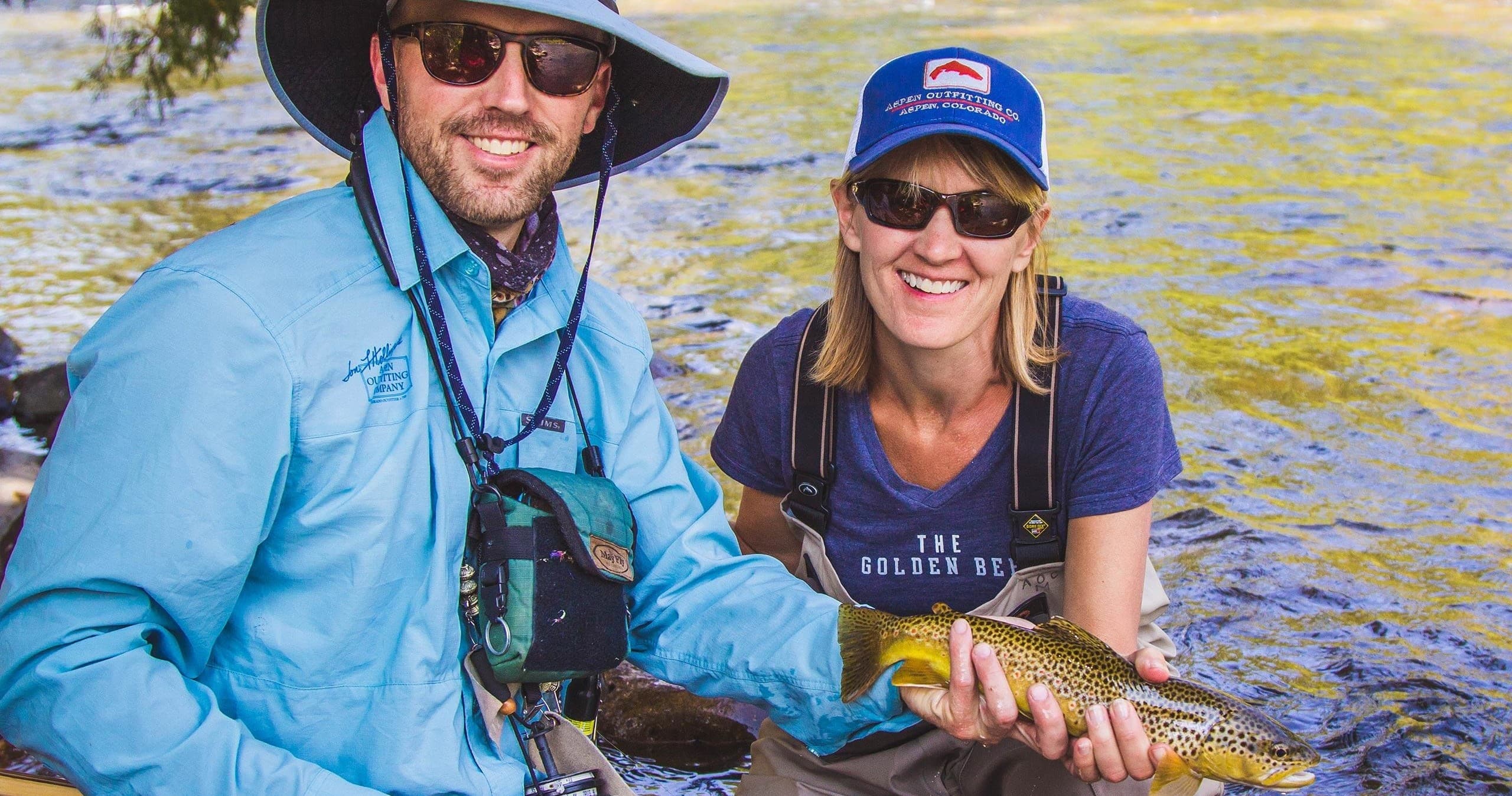 Anglers smiling holding rainbow trout by mountain stream