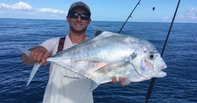 Angler holding large pomfret in open ocean on fishing charter