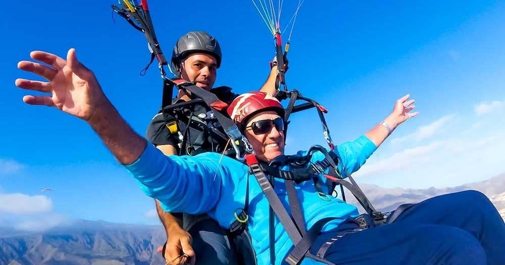 Smiling tandem paragliders against blue sky over Tenerife