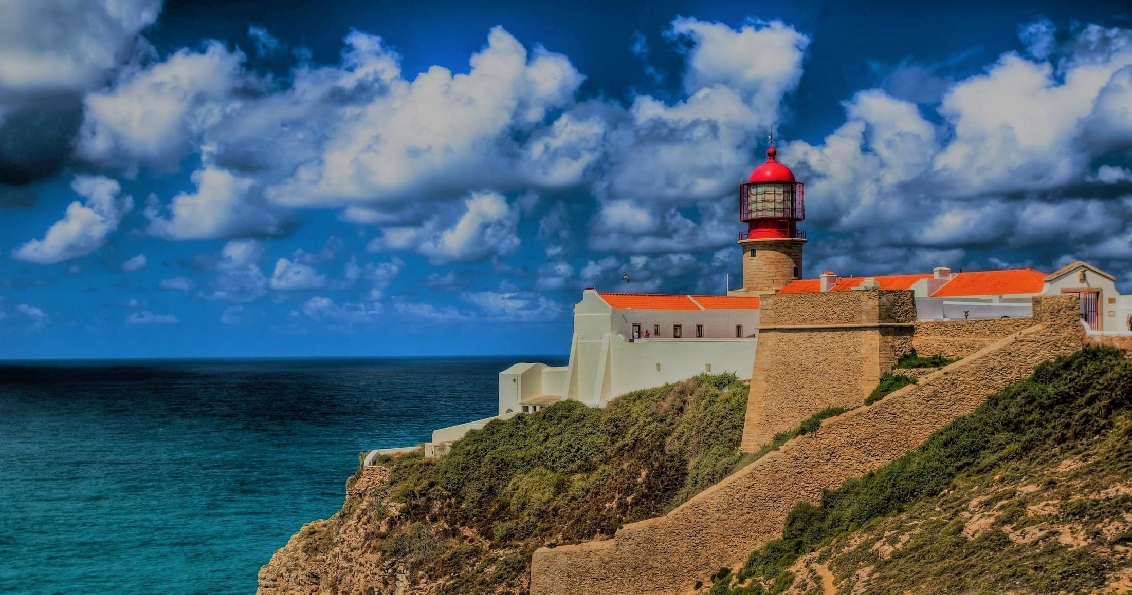 Lighthouse perched on sea cliff under dramatic cloudy skies