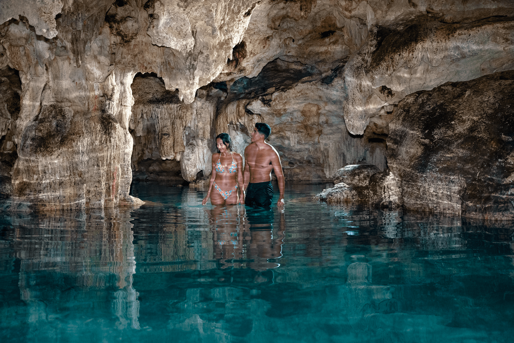 Couple wading in turquoise cenote cave swimming in limestone cavern