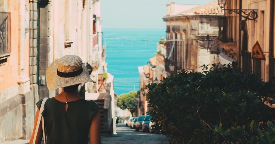 Woman strolling historic Palermo street toward sea view