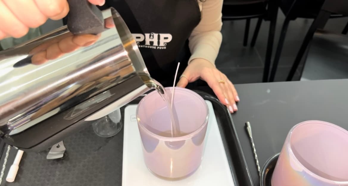 Pouring hot wax into candle jars at indoor studio