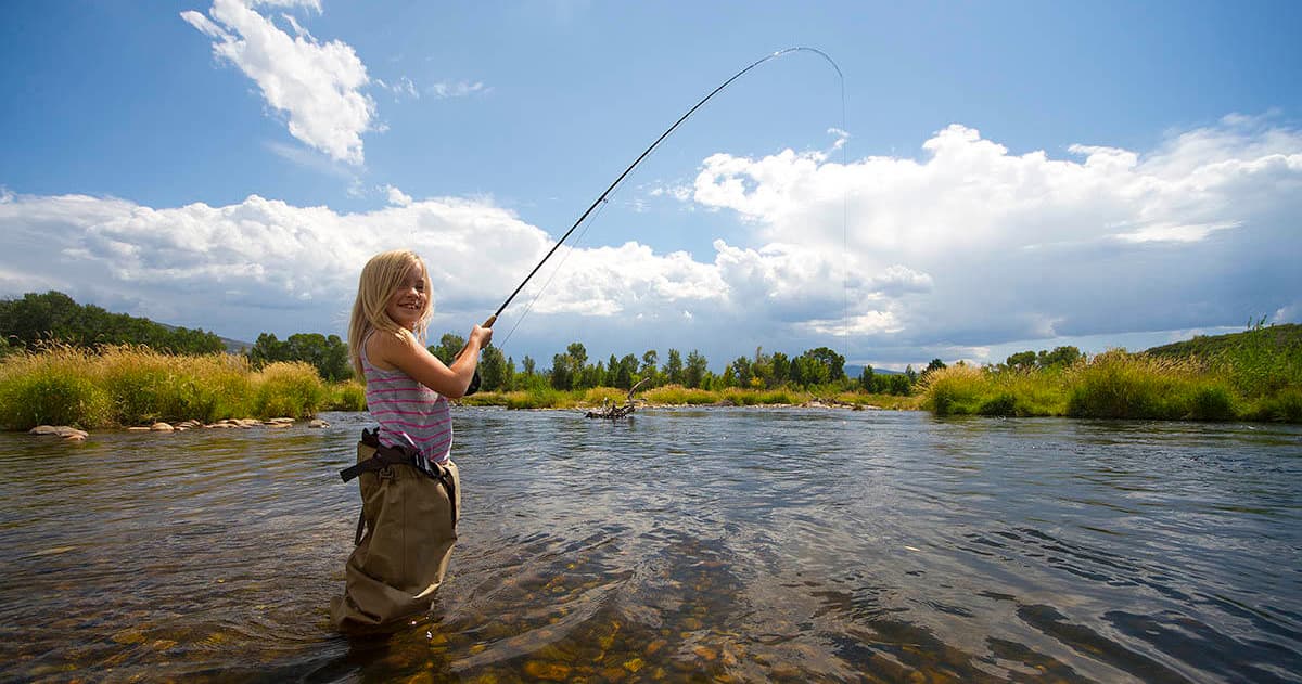 Woman fly fishing in scenic shallow river under blue sky