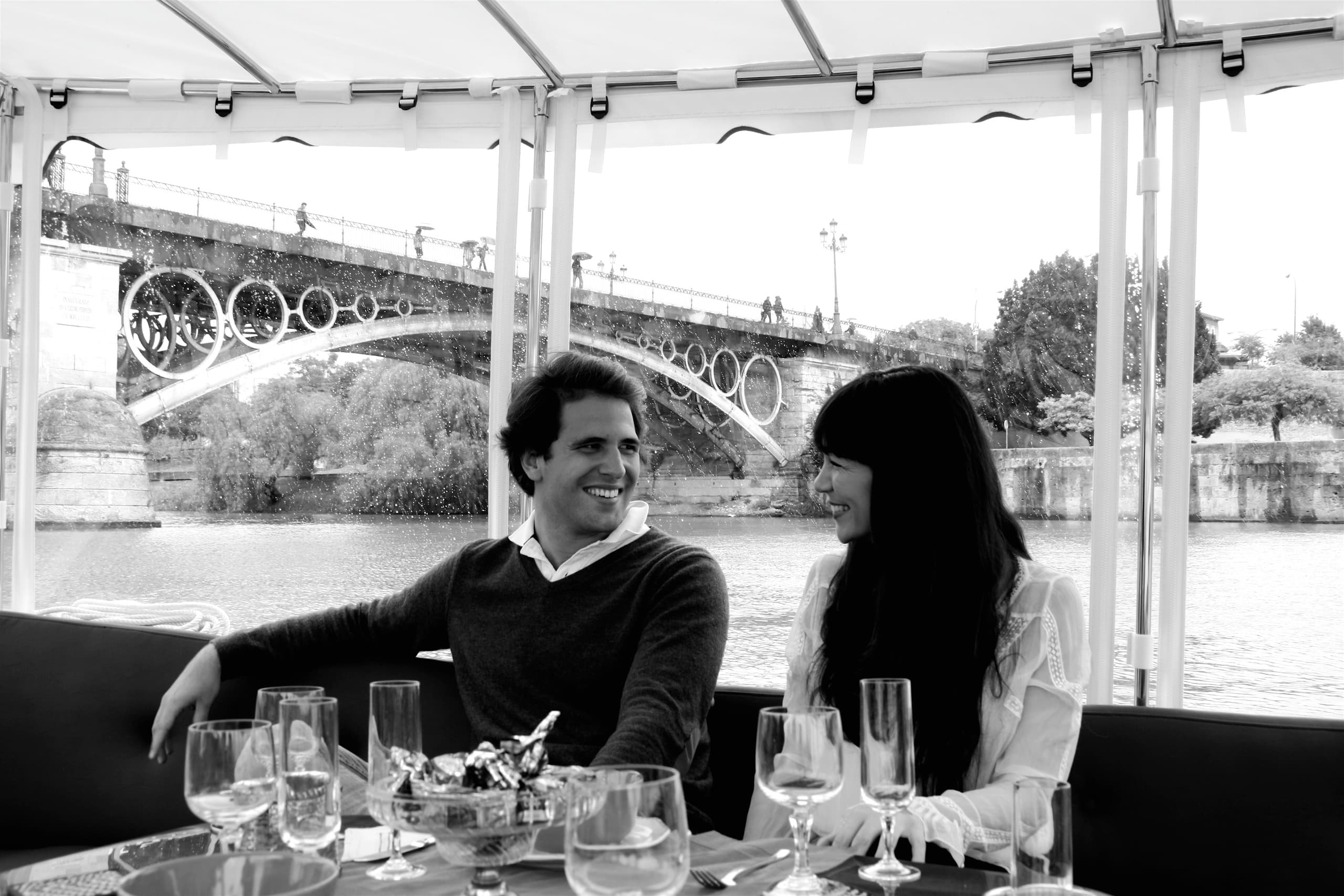 Couple dining aboard a riverboat with bridge backdrop during cruise