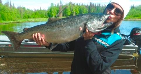 Woman angler holding large salmon on boat in green river, Alaska
