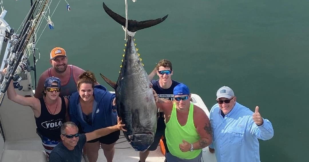 Anglers posing around giant tuna on deck during offshore tuna trip