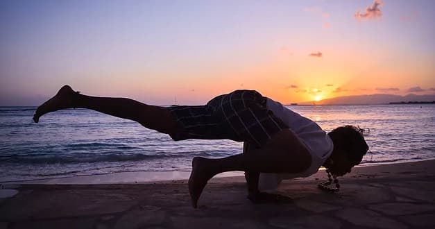 Yoga arm-balance on sandy beach at sunset, ocean horizon