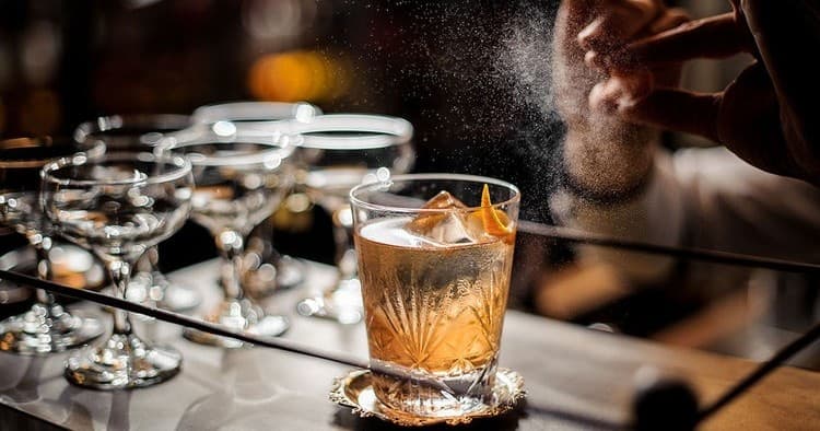 Craft cocktail being garnished at dimly lit bar counter