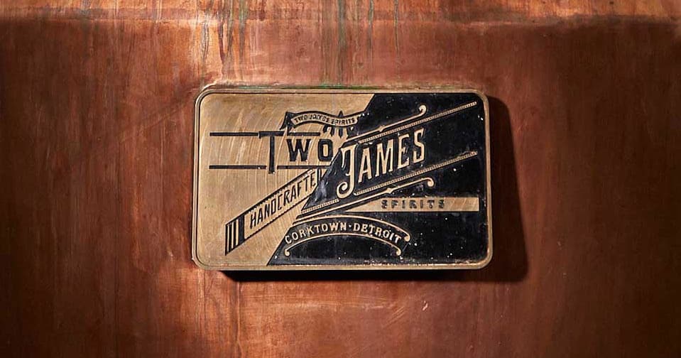 Brass Two James distillery plaque mounted on copper still room wall