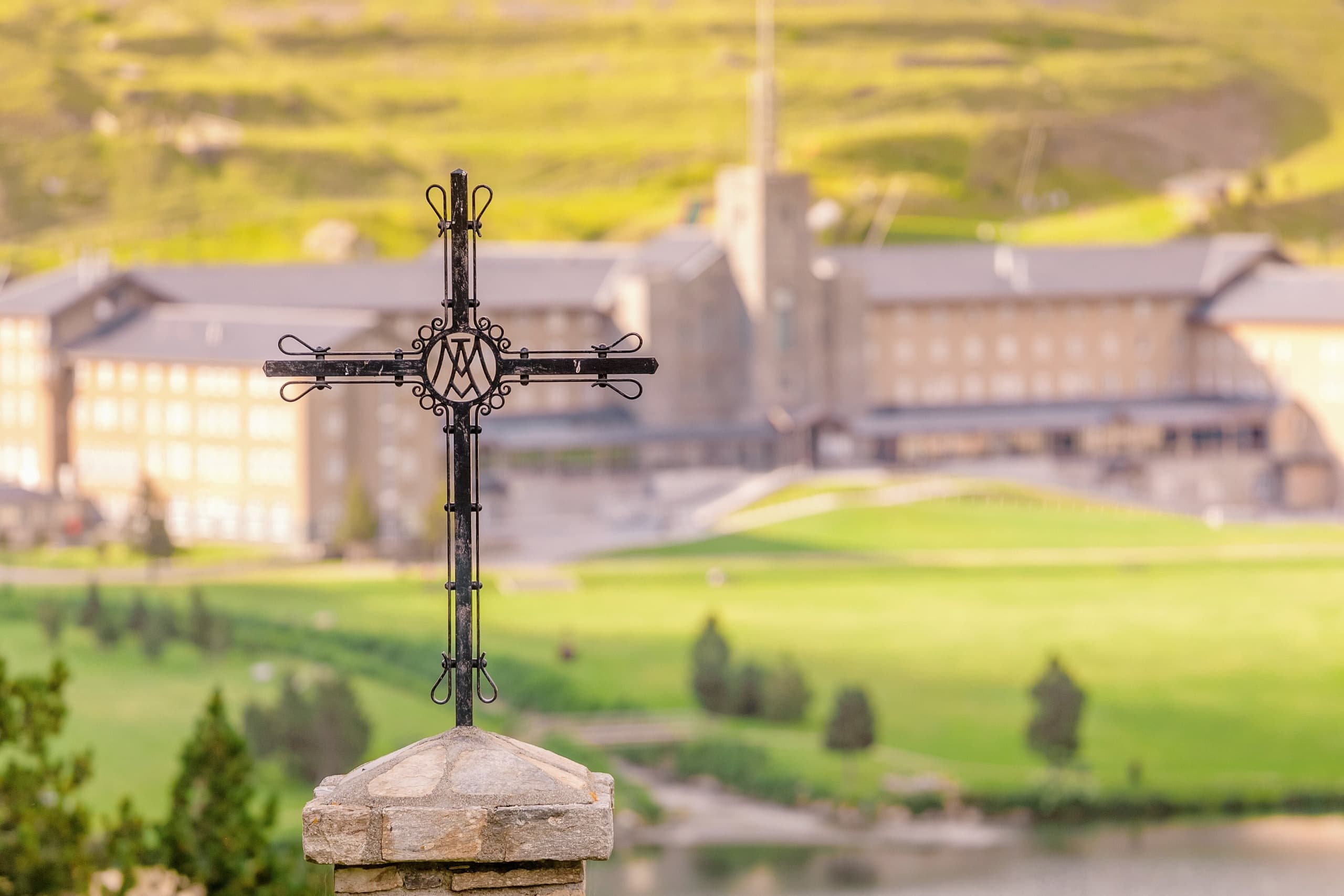 Hilltop iron cross overlooking rural monastery and rolling fields