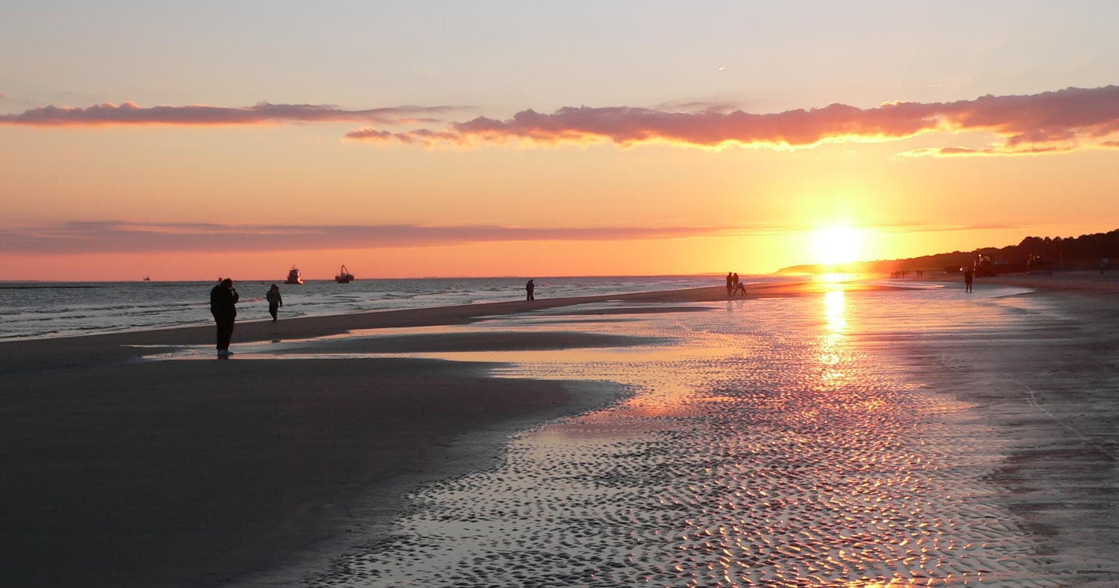 Beach sunset with walkers and reflective tide pools on shoreline