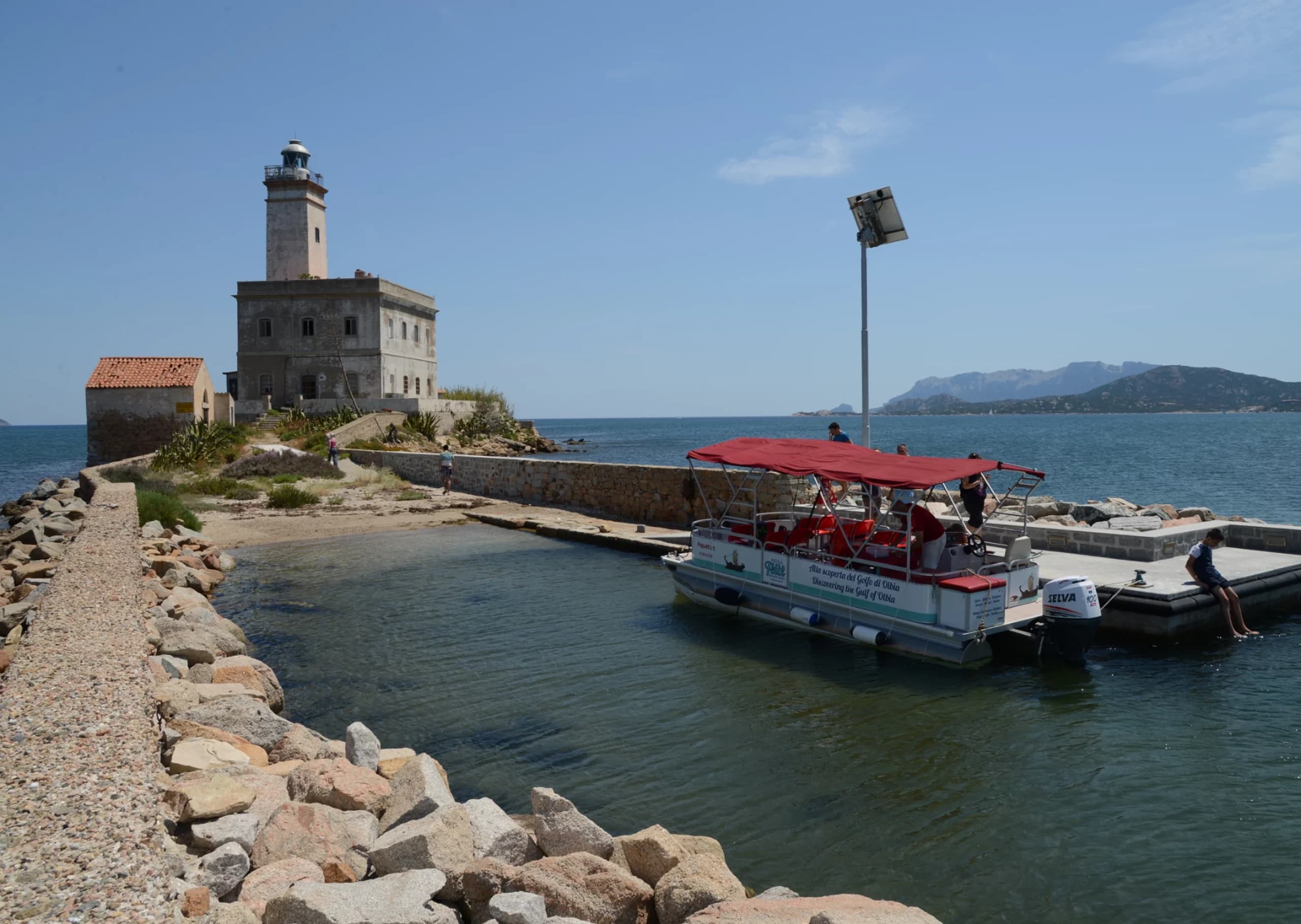 Coastal boat tour docking by historic lighthouse on rocky breakwater