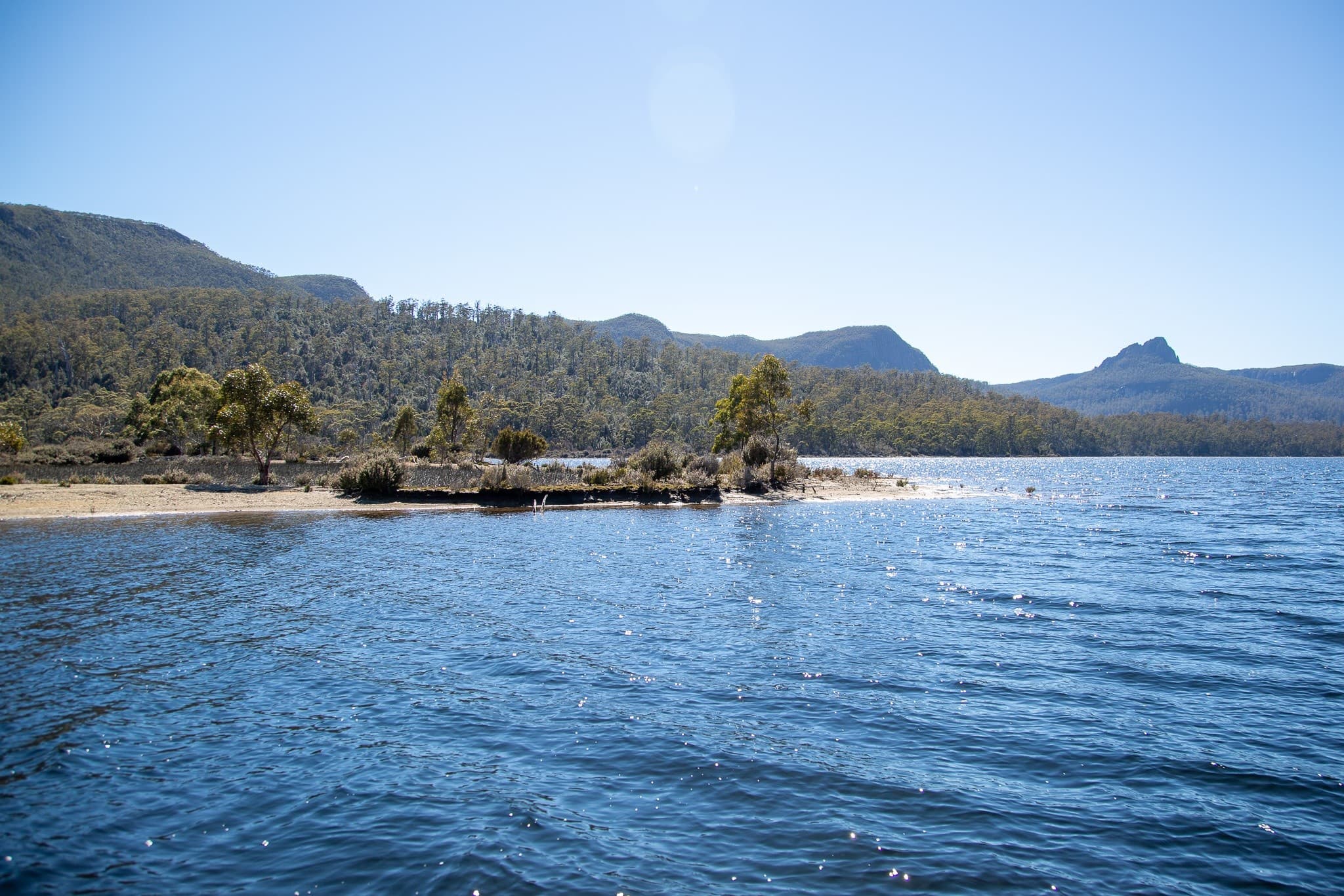 Lake shoreline with small island and distant mountains, calm boating