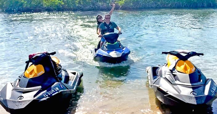 Jet skis on sandy shoreline with riders launching into Florida inlet