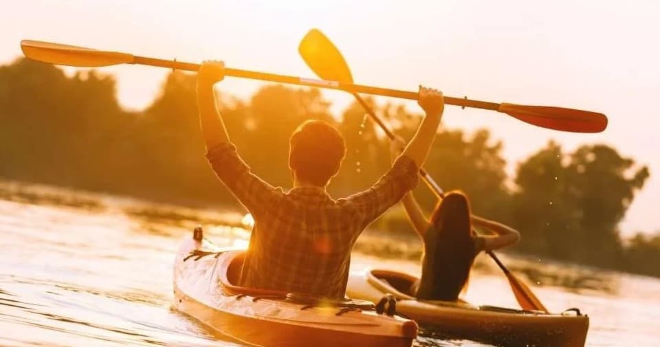 Kayakers raising paddles at sunset on calm river, golden light