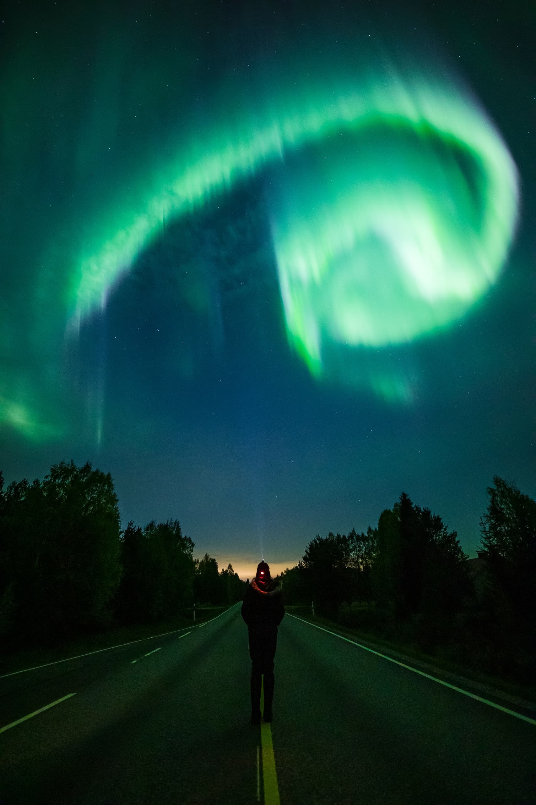 Aurora green bands arching over wooden lakeside cabin at night