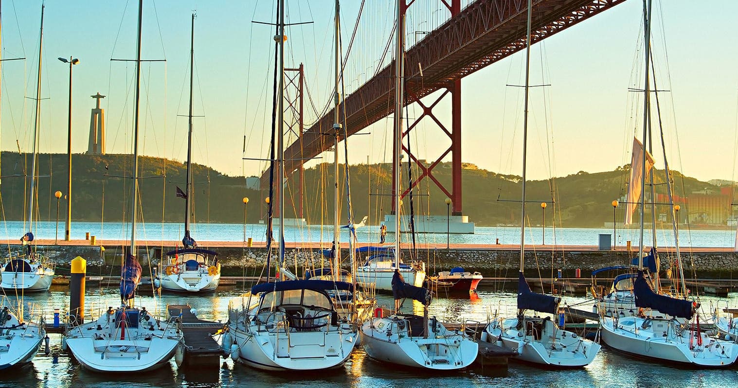 Marina with moored sailboats under Lisbon bridge at golden hour
