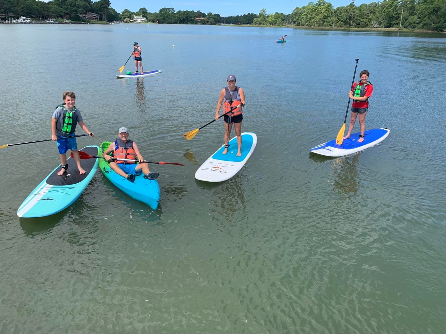 Group paddleboarding and kayaking on a calm, tree-lined lake