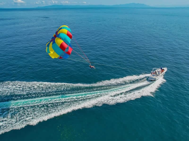 Parasailing over turquoise ocean behind speedboat, coastal adventure