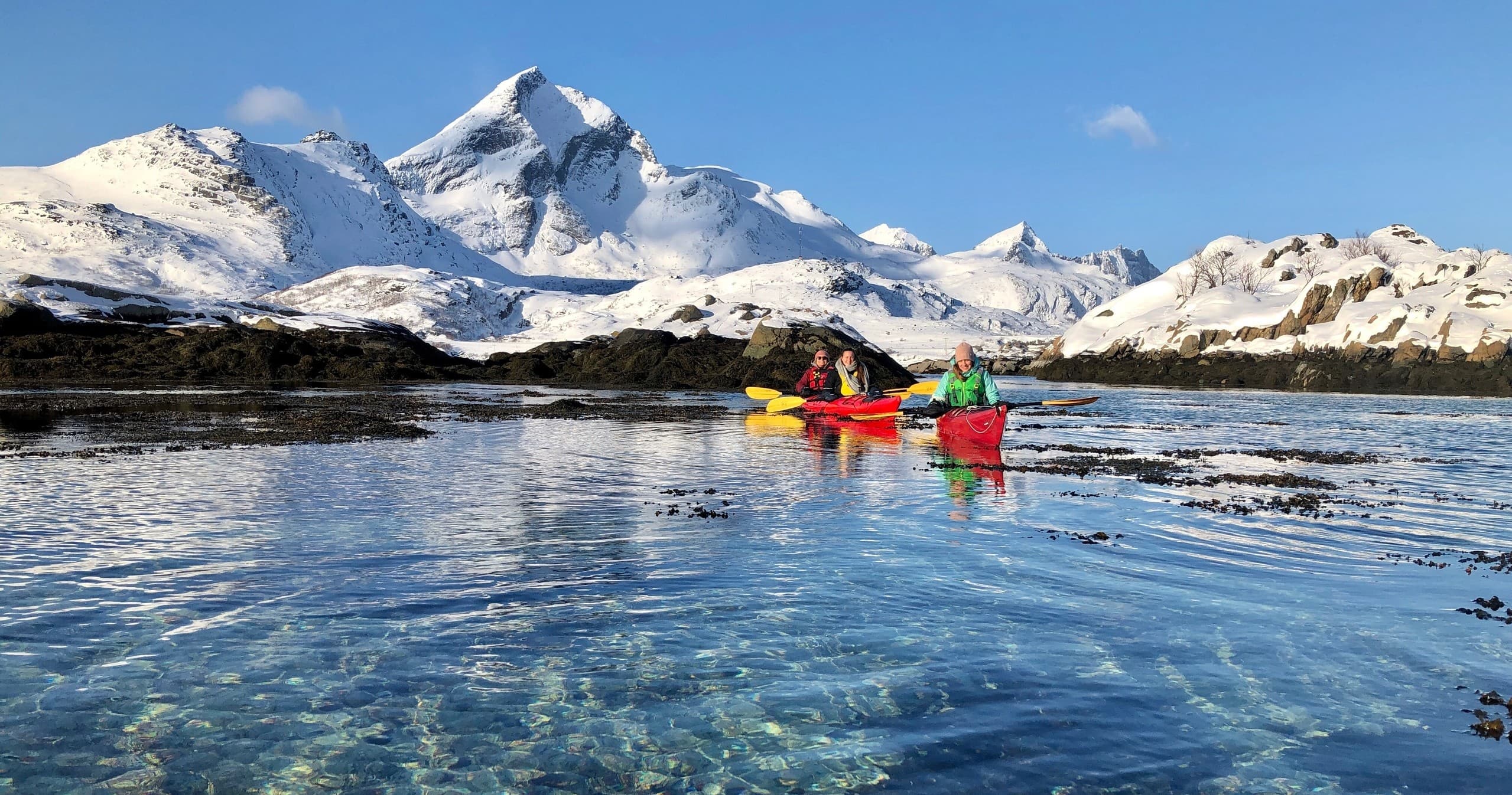 Group kayaking on clear Arctic waters with snowy peaks